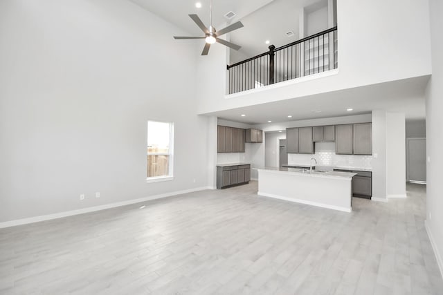 12027 Maple Oak Dr, Houston, TX 77066 - unfurnished living room with a ceiling fan, light wood-style flooring, a towering ceiling, baseboards, and a sink