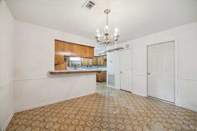 2718 Leichester Dr, Spring, TX 77386 - kitchen featuring brown cabinets, a chandelier, a wainscoted wall, light countertops, and a peninsula