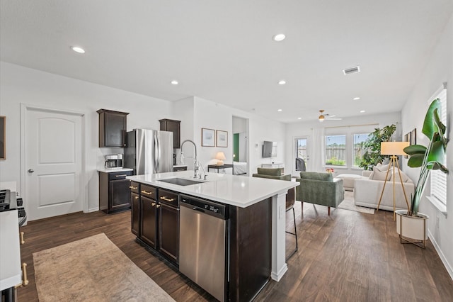 kitchen featuring stainless steel appliances, a sink, light countertops, dark wood-style floors, and a kitchen island with sink
