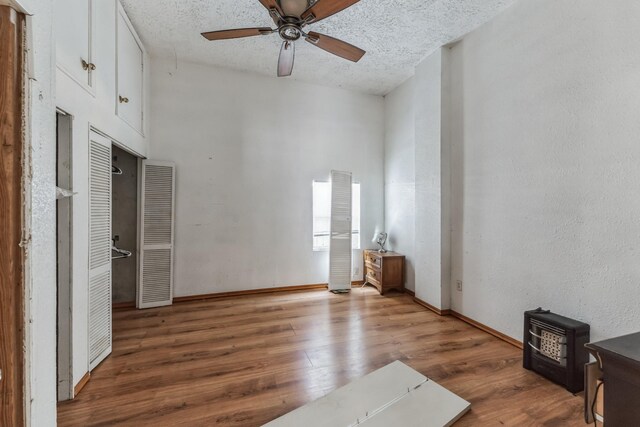 2009 Chestnut St, Houston, TX 77009 - unfurnished living room featuring wood finished floors, ceiling fan, a textured ceiling, a towering ceiling, and a wood stove