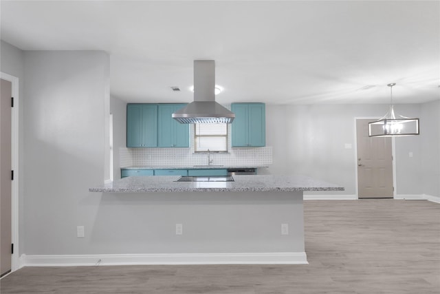 9827 Shive Dr, Houston, TX 77078 - kitchen with blue cabinets, decorative backsplash, island range hood, baseboards, and light wood-style floors