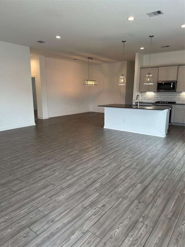 14007 Valley Creek Ct, Conroe, TX 77384 - kitchen featuring stainless steel microwave, open floor plan, dark countertops, dark wood finished floors, and gray cabinetry