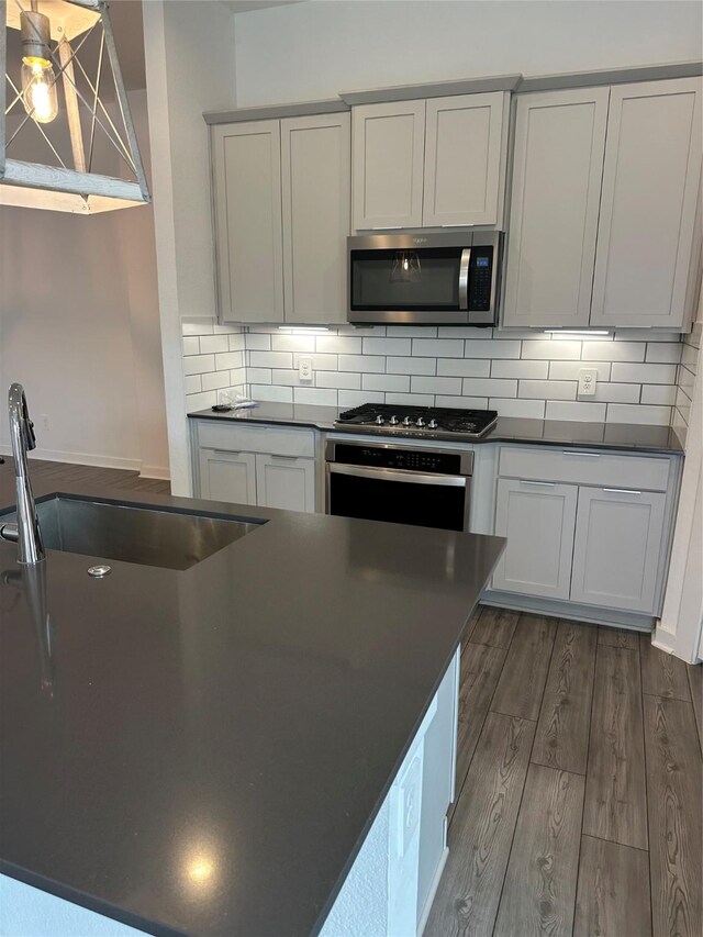 14007 Valley Creek Ct, Conroe, TX 77384 - kitchen featuring appliances with stainless steel finishes, dark countertops, dark wood-type flooring, decorative backsplash, and a sink