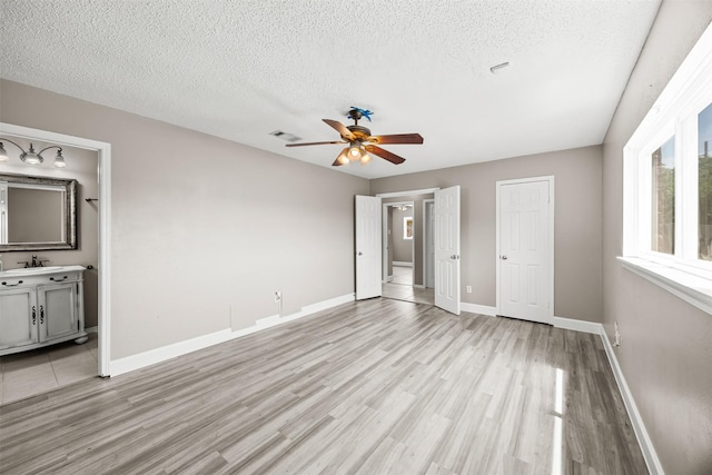 1043 Sierra Shadows Dr, Katy, TX 77450 - unfurnished bedroom featuring light wood-type flooring, a textured ceiling, baseboards, ensuite bath, and a sink