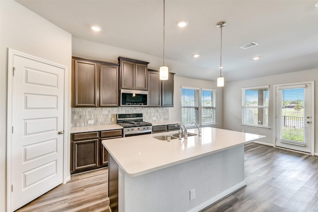 1210 Oak Barrel Run, Richmond, TX 77406 - kitchen with appliances with stainless steel finishes, a sink, backsplash, light wood finished floors, and a kitchen island with sink