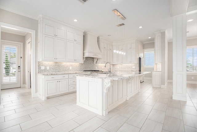 11503 Kings Point Blvd, Mont Belvieu, TX 77535 - kitchen with custom range hood, crown molding, tasteful backsplash, a kitchen island with sink, and a sink