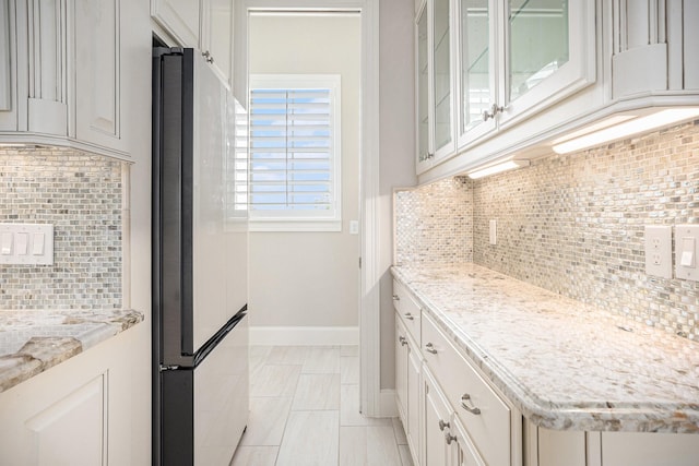11503 Kings Point Blvd, Mont Belvieu, TX 77535 - kitchen with freestanding refrigerator, decorative backsplash, baseboards, glass insert cabinets, and light stone counters
