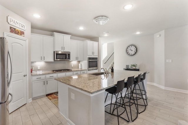 5010 Trembling Aspen Ln, Rosenberg, TX 77471 - kitchen with appliances with stainless steel finishes, a sink, a kitchen bar, decorative backsplash, and a kitchen island with sink