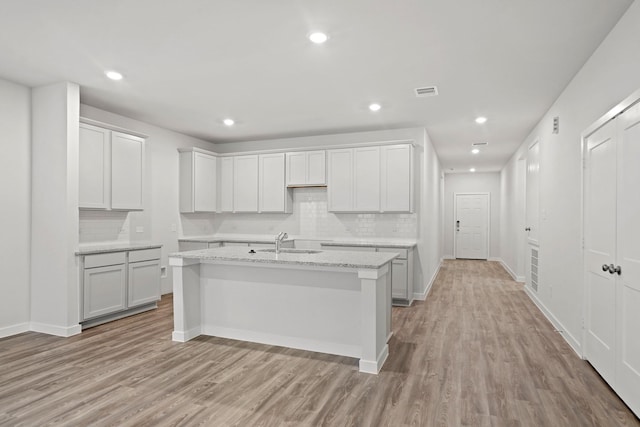 18523 Lilliput Ln, New Caney, TX 77357 - kitchen featuring light wood-style floors, a center island with sink, a sink, backsplash, and baseboards