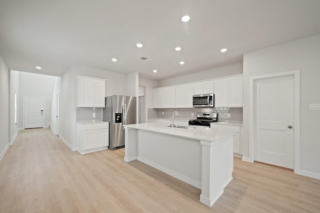 7919 Grand Louis Way, Spring, TX 77379 - kitchen with appliances with stainless steel finishes, backsplash, light countertops, light wood-style flooring, and an island with sink