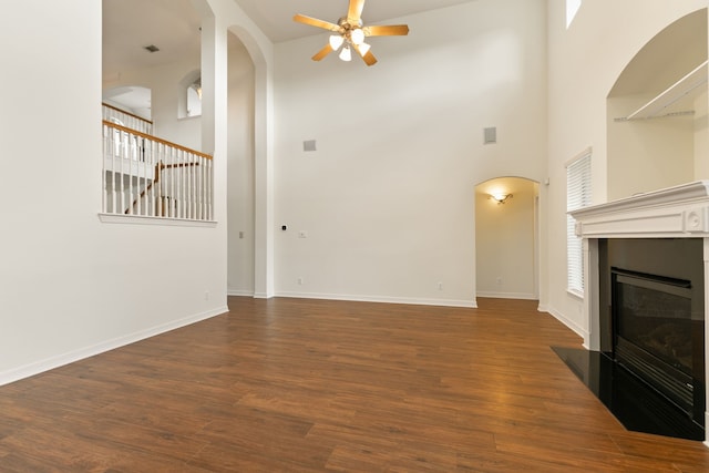 15106 Aragon Green Dr, Cypress, TX 77433 - unfurnished living room with a ceiling fan, a towering ceiling, arched walkways, a fireplace with flush hearth, and dark wood finished floors