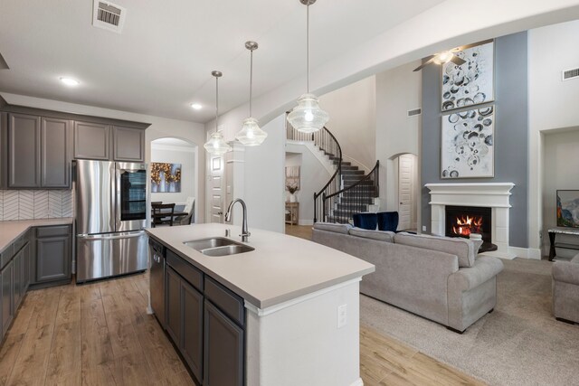 17505 Spice Merlot Ln, Conroe, TX 77302 - kitchen with appliances with stainless steel finishes, a sink, arched walkways, a warm lit fireplace, and light countertops