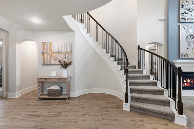 17505 Spice Merlot Ln, Conroe, TX 77302 - stairs with arched walkways, wood finished floors, baseboards, a warm lit fireplace, and a high ceiling
