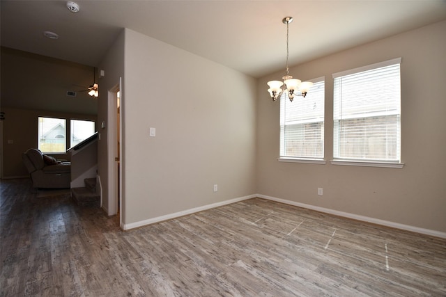 empty room featuring wood finished floors, healthy amount of natural light, a chandelier, and ceiling fan