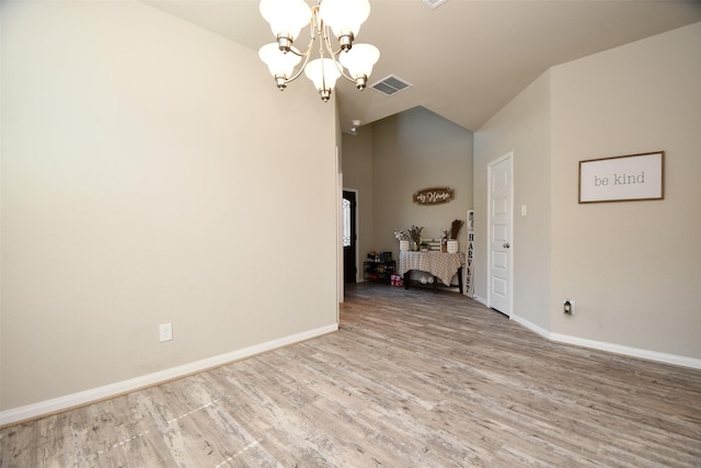 spare room with a chandelier, vaulted ceiling, wood finished floors, and baseboards