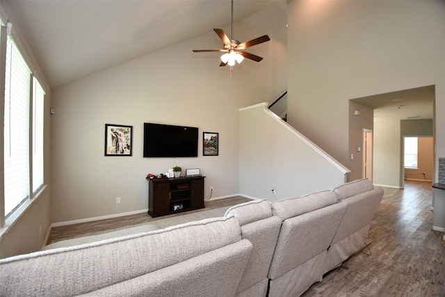 living room featuring high vaulted ceiling, wood finished floors, ceiling fan, stairway, and baseboards