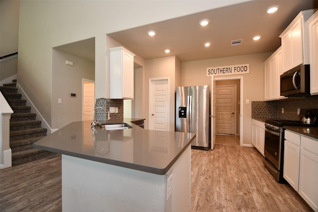 kitchen featuring appliances with stainless steel finishes, a sink, dark countertops, light wood-style flooring, and a peninsula