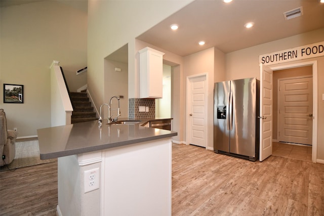 kitchen with stainless steel refrigerator with ice dispenser, a sink, white cabinets, light wood-style flooring, and dark countertops