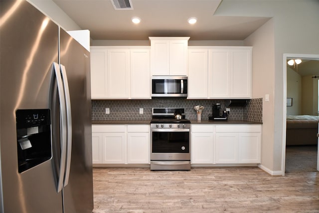 kitchen with appliances with stainless steel finishes, dark countertops, light wood-style floors, tasteful backsplash, and white cabinets