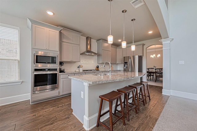16826 Ellicott Rock Dr, Humble, TX 77346 - kitchen featuring stainless steel appliances, wall chimney range hood, dark wood-type flooring, a sink, and an island with sink
