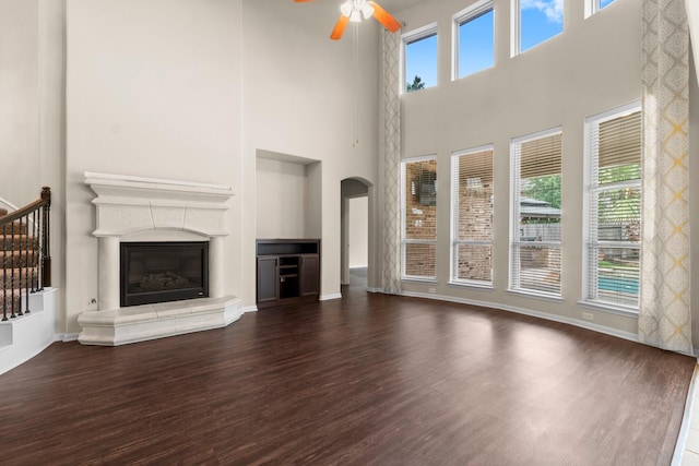 27303 Balson Forest Ln, Spring, TX 77386 - unfurnished living room with wood finished floors, a ceiling fan, arched walkways, a high ceiling, and a glass covered fireplace