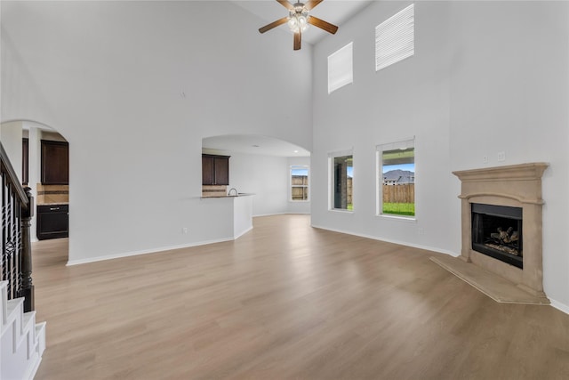 11915 Eagle Ridge Dr, Mont Belvieu, TX 77535 - unfurnished living room with arched walkways, ceiling fan, a fireplace with raised hearth, stairs, and light wood-type flooring