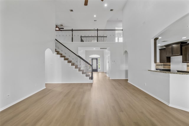 11915 Eagle Ridge Dr, Mont Belvieu, TX 77535 - unfurnished living room with a ceiling fan, arched walkways, stairs, light wood-style flooring, and a high ceiling
