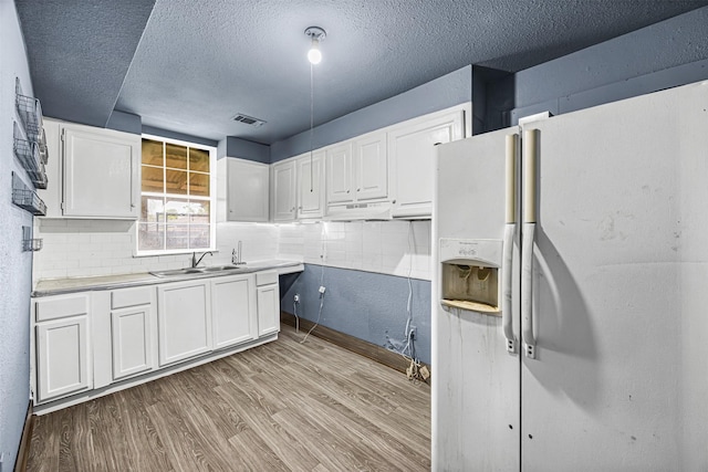 12910 Green River Dr, Houston, TX 77044 - kitchen featuring white refrigerator with ice dispenser, a sink, white cabinetry, light wood-style floors, and a textured ceiling