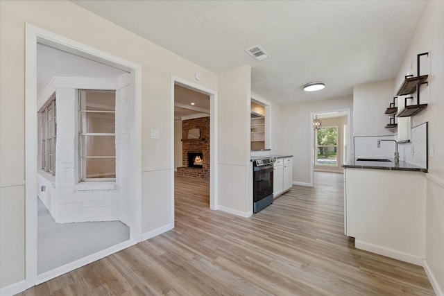9863 Swan Ct, Conroe, TX 77385 - kitchen with electric range, a fireplace, light wood-style floors, and white cabinetry