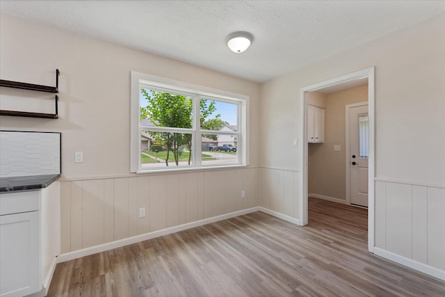 9863 Swan Ct, Conroe, TX 77385 - unfurnished dining area with light wood-style flooring, wainscoting, and a textured ceiling