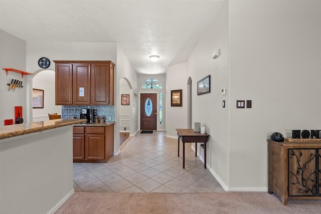 411 Ceole Ln, League City, TX 77573 - kitchen with arched walkways, light tile patterned flooring, backsplash, stone counters, and brown cabinetry