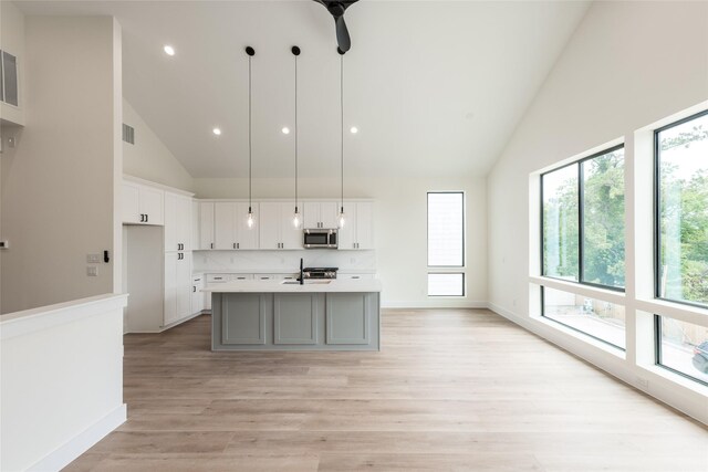 6137 Pacific Forest Dr, Houston, TX 77346 - kitchen with stainless steel microwave, high vaulted ceiling, light countertops, white cabinetry, and light wood-style floors