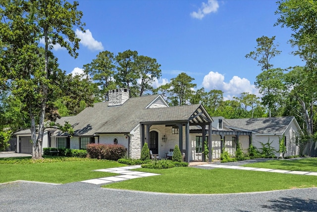 view of front facade featuring a front yard, a chimney, stone siding, and an attached garage