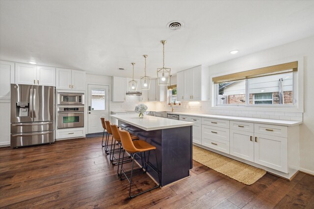3006 Ann Arbor Dr, Houston, TX 77063 - kitchen with appliances with stainless steel finishes, a breakfast bar area, dark wood-style flooring, white cabinetry, and recessed lighting