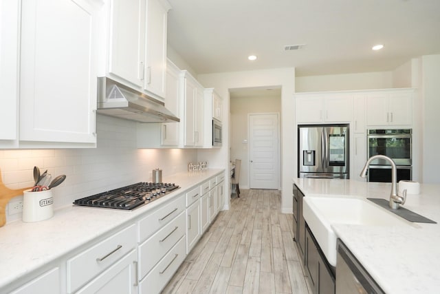 10134 Blythe St, Rosharon, TX 77583 - kitchen with appliances with stainless steel finishes, under cabinet range hood, white cabinetry, light wood-type flooring, and recessed lighting