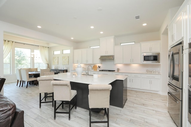 10134 Blythe St, Rosharon, TX 77583 - kitchen with stainless steel appliances, a breakfast bar, light wood-type flooring, white cabinetry, and under cabinet range hood