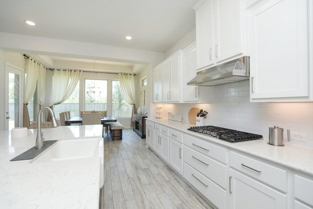 10134 Blythe St, Rosharon, TX 77583 - kitchen with under cabinet range hood, stainless steel gas cooktop, a sink, white cabinetry, and tasteful backsplash