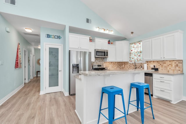 4019 Ector Dr, Galveston, TX 77554 - kitchen with stainless steel appliances, light wood-style flooring, backsplash, white cabinets, and lofted ceiling
