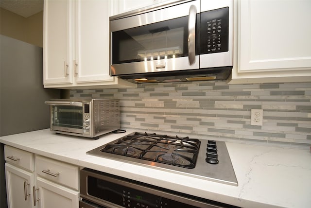 19026 Rustling Ridge Ln, Tomball, TX 77377 - kitchen featuring appliances with stainless steel finishes, decorative backsplash, white cabinetry, and light stone counters