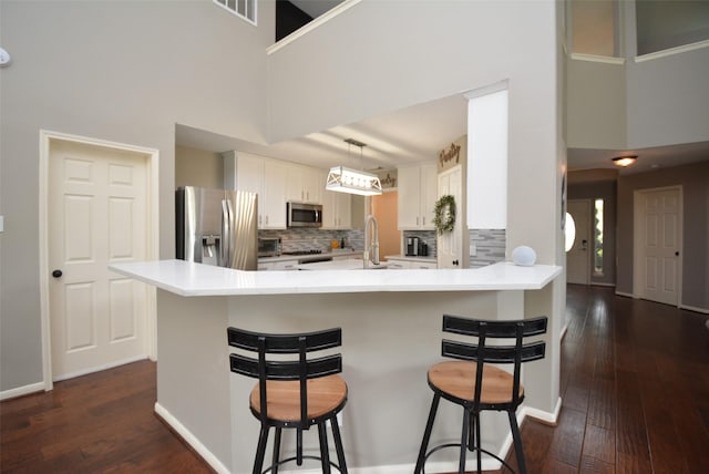 19026 Rustling Ridge Ln, Tomball, TX 77377 - kitchen featuring appliances with stainless steel finishes, dark wood-type flooring, a towering ceiling, a peninsula, and backsplash