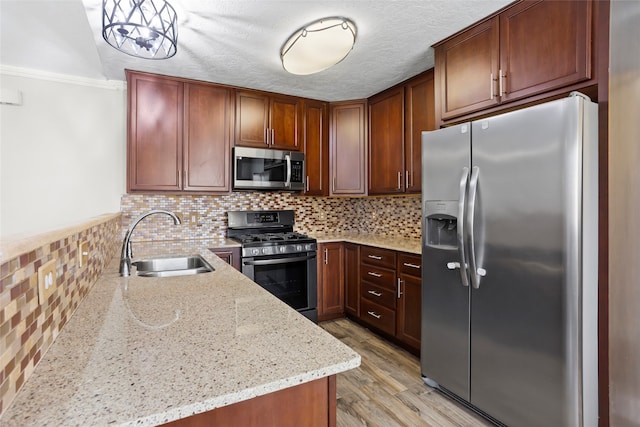 5000 Old Castle Ln, Dickinson, TX 77539 - kitchen with stainless steel appliances, a sink, light stone countertops, light wood finished floors, and a peninsula