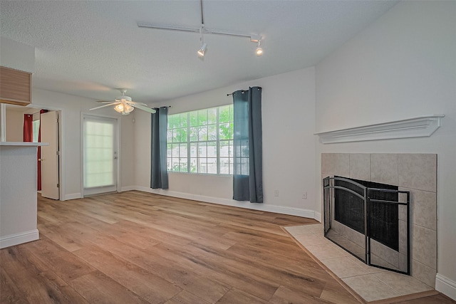 2750 Holly Hall St Unit 910, Houston, TX 77054 - unfurnished living room featuring light wood-style floors, a tile fireplace, a ceiling fan, rail lighting, and a textured ceiling