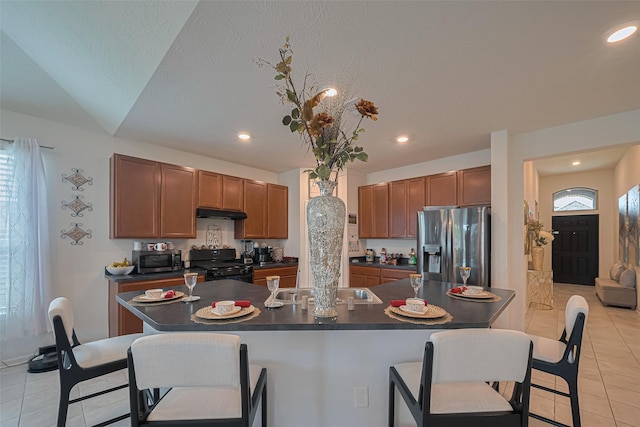 15602 Clearwater Bend Dr, Houston, TX 77044 - kitchen featuring appliances with stainless steel finishes, dark countertops, light tile patterned floors, a breakfast bar, and under cabinet range hood