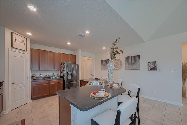 15602 Clearwater Bend Dr, Houston, TX 77044 - kitchen with stainless steel refrigerator with ice dispenser, a sink, light tile patterned floors, a breakfast bar area, and dark countertops