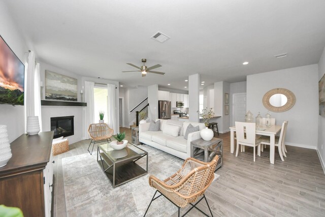 2142 Emerald Diamond Ct, Fresno, TX 77545 - living area with a glass covered fireplace, stairs, light wood finished floors, a ceiling fan, and baseboards