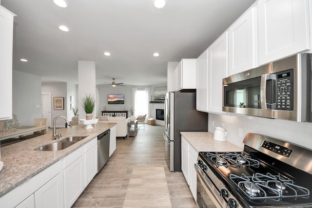 2142 Emerald Diamond Ct, Fresno, TX 77545 - kitchen featuring appliances with stainless steel finishes, a sink, a glass covered fireplace, open floor plan, and ceiling fan