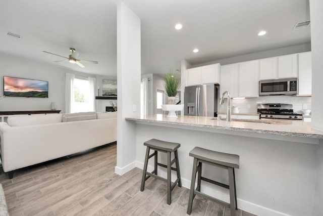 2142 Emerald Diamond Ct, Fresno, TX 77545 - kitchen with appliances with stainless steel finishes, light stone counters, a kitchen bar, white cabinetry, and a ceiling fan