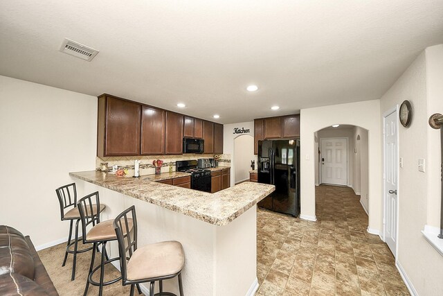 15319 Meandering Post Trl, Houston, TX 77044 - kitchen with black appliances, arched walkways, a peninsula, a breakfast bar, and tasteful backsplash