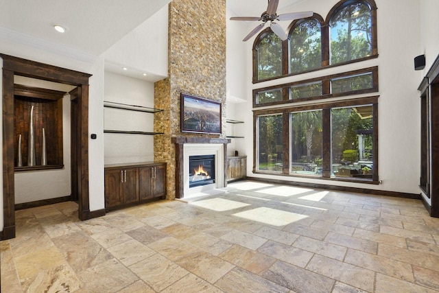 20806 Kings Crown Ct, Humble, TX 77346 - unfurnished living room featuring stone tile floors, a towering ceiling, a glass covered fireplace, baseboards, and a ceiling fan