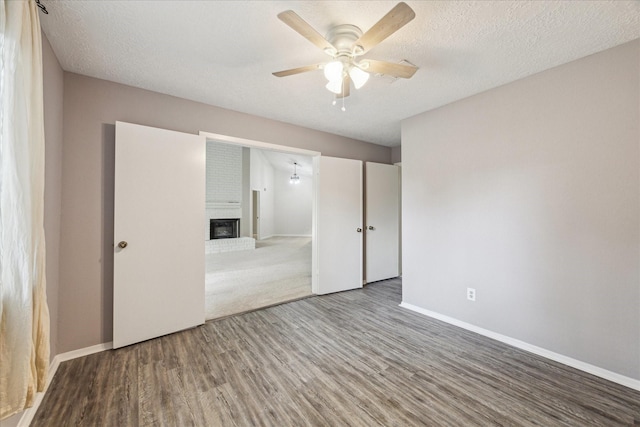 1018 W Castlewood Ave, Friendswood, TX 77546 - unfurnished bedroom featuring wood finished floors, baseboards, a fireplace, a textured ceiling, and a ceiling fan